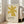 May include: Framed poster featuring a yellow star-like abstract shape on cream textured background with "ELLSWORTH KELLY" and "Aloes, 1958" text below. Natural wood frame leaning against white wall beside beige upholstered sofa in bright living room with large windows and natural light streaming across wooden floors.