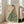 May include: Framed art print leaning against white wall beside beige sofa, showing woman in green striped kimono with coral floral sleeve holding orange persimmon, rendered in soft Japanese illustration style on cream background, displayed in light wooden frame in bright sunlit room with hardwood floors.