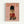 Framed poster featuring a small Pomeranian dog dressed as a British Royal Guard in a red military jacket with gold braiding, black fur hat, and tiny black boots. The dog sits against a soft pink background with "DOGUE" text in orange letters at the top, displayed in a light wood frame on a white wall.