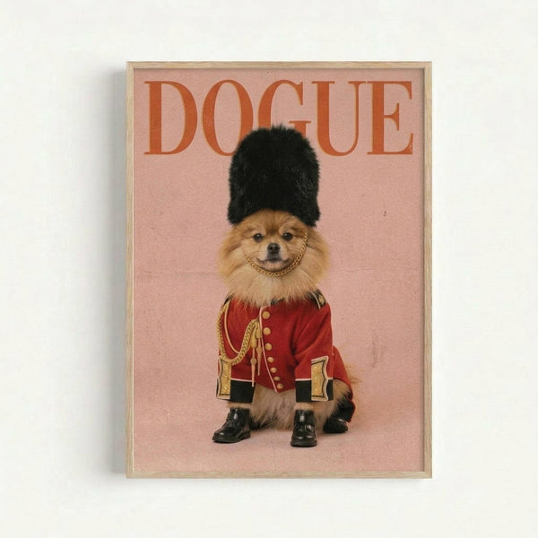 Framed poster featuring a small Pomeranian dog dressed as a British Royal Guard in a red military jacket with gold braiding, black fur hat, and tiny black boots. The dog sits against a soft pink background with "DOGUE" text in orange letters at the top, displayed in a light wood frame on a white wall.