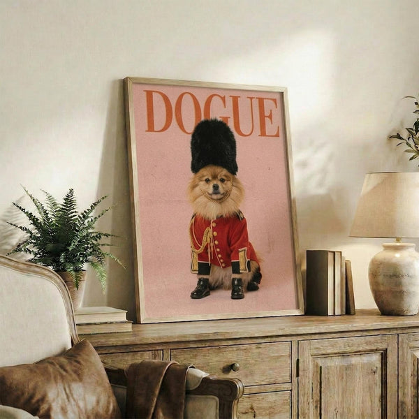 May include: Framed poster with pink background featuring a fluffy Pomeranian dog wearing a red military guard uniform with gold buttons and black fur hat, displayed on rustic wooden sideboard alongside potted fern, ceramic vase, stacked books, and beige upholstered chair in neutral-toned living room setting.