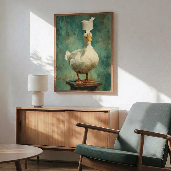 May include: A framed artwork showing a white duck balancing a toilet paper roll on its head, painted in realistic style against a teal-green textured background. The poster hangs above a mid-century modern wooden credenza with a white ceramic table lamp. A sage green upholstered armchair with wooden frame sits nearby on a round wooden coffee table, all in a bright room with white walls and natural sunlight casting shadows.
