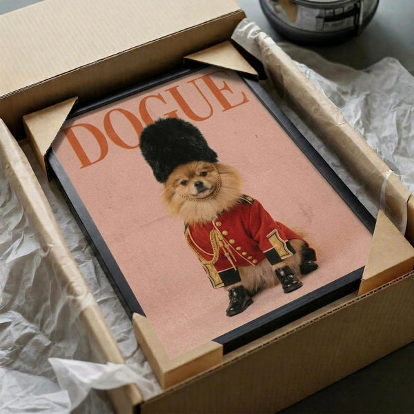 May include: Framed poster print being unpacked from brown cardboard box with tissue paper. Print features fluffy Pomeranian dog dressed as British Royal Guard in red military uniform with gold braiding and tall black bearskin hat against pink background. Text "DOGUE" appears in orange letters. Black frame visible inside packaging materials on white surface.