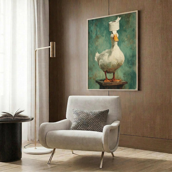 May include: Framed poster print hanging on wood-paneled wall showing white duck balancing toilet paper roll on head, standing on wooden platform against teal-green painted background. Modern living room setting with beige upholstered armchair, geometric patterned pillow, brass floor lamp, and dark round side table with open book.