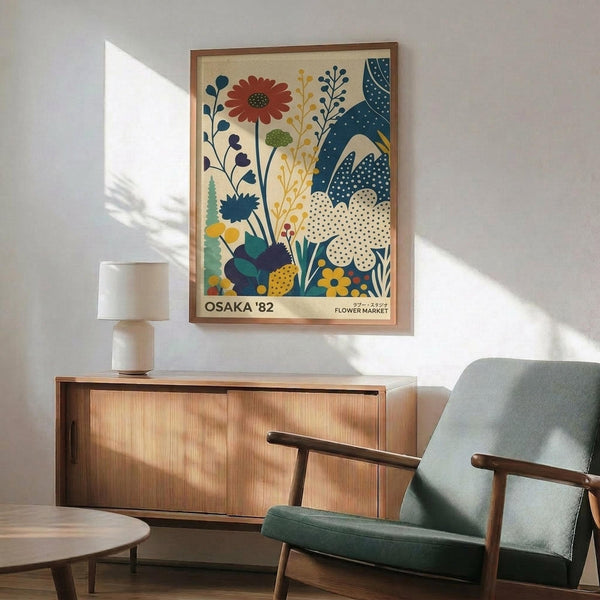 May include: Framed vintage-style botanical poster featuring colorful illustrated flowers and plants in blues, oranges, and greens with "OSAKA '82 FLOWER MARKET" text, displayed above a wooden sideboard with white ceramic lamp in modern living room setting with teal upholstered chair and wooden coffee table.