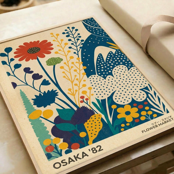 May include: Vintage-style poster print with colorful illustrated flowers and plants in orange, blue, yellow, and green. Features stylized botanical elements including daisies, leaves, and dotted mushroom shapes against cream background. Text reads "OSAKA '82" and "FLOWER MARKET" in bottom corners. Print shown on wooden surface with rolled white paper in background.