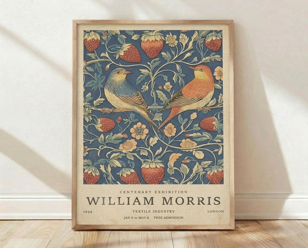 May include: Framed vintage exhibition poster featuring two colorful birds perched among strawberry plants with red berries and flowing vines on deep blue background. Light wood frame sits on wooden floor against white wall with natural lighting casting soft shadows.