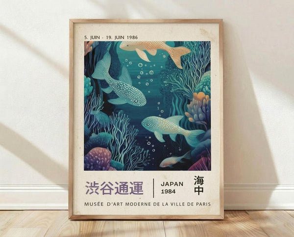 May include: Framed vintage exhibition poster featuring underwater scene with whales, coral, and sea plants in turquoise and teal tones. Japanese text and "JAPAN 1984" visible below artwork. Light wooden frame displayed against white textured wall on wooden floor with soft natural lighting creating shadows.