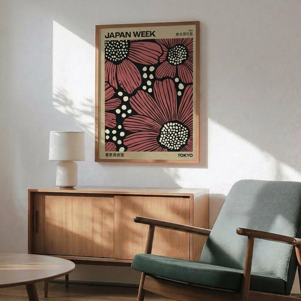 May include: Framed vintage Japanese poster with large pink flowers and white dotted centers on dark background, displayed above wooden sideboard with small white table lamp. Mid-century modern green upholstered chair with wooden arms sits nearby in bright, minimalist room with white walls and natural sunlight creating geometric shadows.