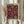 May include: Person in cream knit sweater holding a framed vintage exhibition poster featuring stylized pink and coral flowers with white polka dot centers on black background. The poster displays "JAPAN WEEK" at top with Japanese characters and "TOKYO" at bottom. Natural wood frame, soft lighting, dried wheat stems visible to left, neutral curtained background.