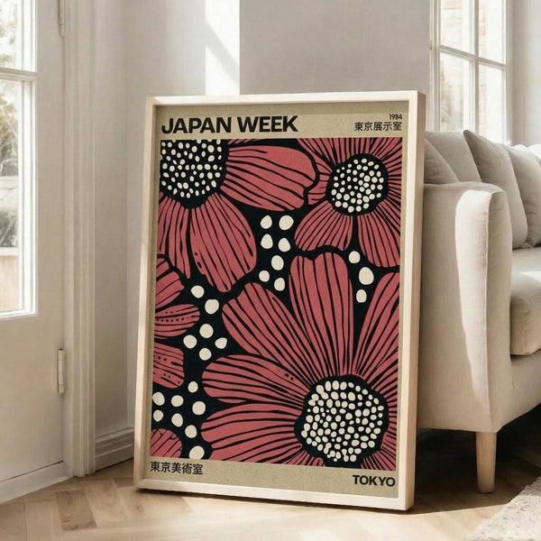 May include: Framed vintage-style poster with pink and black floral design featuring stylized sunflowers and polka dot patterns, displayed against white wall next to beige upholstered chair in bright modern living room with large windows and natural lighting.