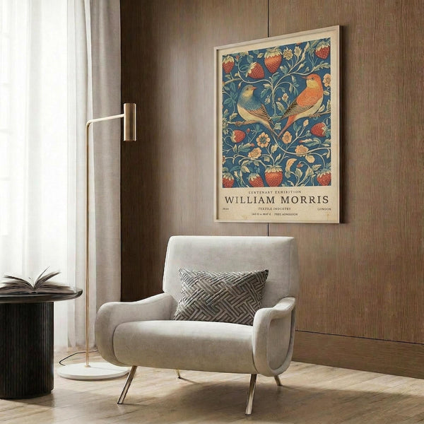 May include: Framed vintage William Morris exhibition poster featuring two orange and yellow birds perched among blue foliage, red strawberries, and cream flowers. Poster hangs on wood paneled wall above cream upholstered armchair with geometric pillow. Modern floor lamp and side table with open book complete the warm, sophisticated reading nook setting.