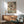 May include: Framed vintage-style illustration of two detailed fish with pink fins swimming among green aquatic plants and bubbles, displayed above a wooden sideboard with lamp in modern living room setting with sage green upholstered chair and round coffee table
