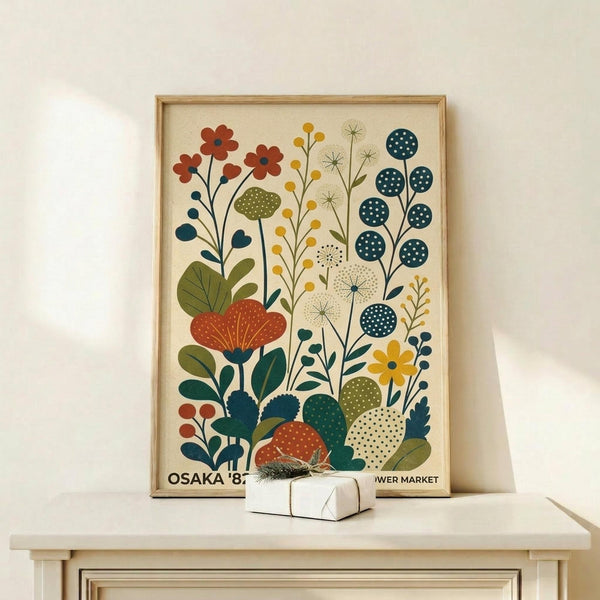 May include: Framed botanical print featuring stylized flowers, mushrooms, and plants in rust orange, teal blue, olive green, and mustard yellow against cream background, displayed on light wood shelf next to small white wrapped gift with evergreen sprig, natural wood frame, modern folk art illustration style.