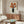 May include: Framed botanical print featuring orange poppies in black vase displayed above wooden sideboard in modern living room. White curved chair and glass-top coffee table visible. Artwork shows vintage Japanese woodblock style with cream background and natural wood frame.