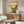 May include: Japanese woodblock print artwork featuring a bird perched on orange trumpet vine flowers with mountains and traditional architecture in background, displayed in thin frame above mid-century modern walnut credenza in minimalist living room with cream walls, white sculptural chair, glass-top coffee table, and warm natural lighting