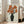 May include: Large framed botanical print leaning against white wall next to beige upholstered chair. Artwork shows orange-red poppies with dark centers in black vase against wood grain background, featuring Japanese woodblock print style with visible artist seal. Natural light streams through windows creating soft shadows on hardwood floor.