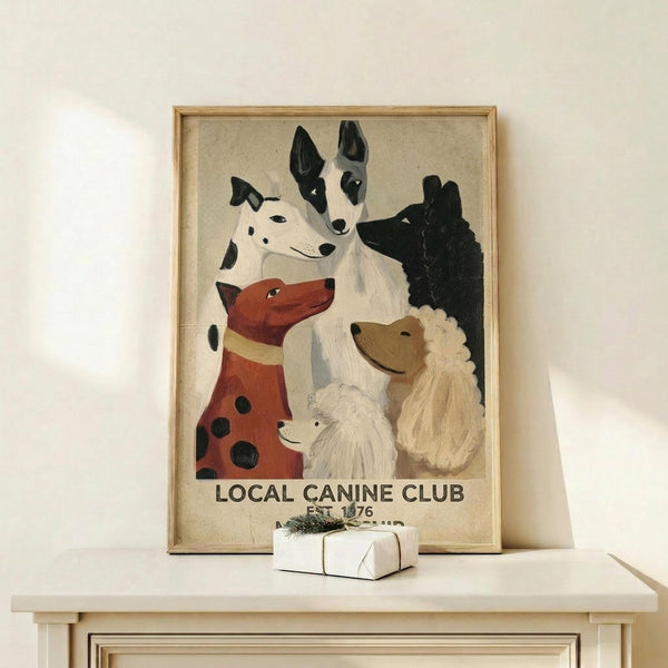 May include: Framed vintage-style poster featuring seven painted dog portraits in various breeds and colors including black, white, brown, and reddish-brown dogs arranged in a group composition. Text reads "LOCAL CANINE CLUB EST. 1976" at bottom on cream background. Light wood frame sits on white shelf against white wall next to small wrapped gift box with twine and greenery.