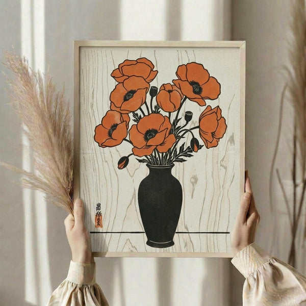 May include: Person in cream ruffled blouse holding framed botanical art print featuring orange poppies in dark vase against wood grain background, displayed in light wooden frame. Left hand holds dried wheat stems. Neutral curtained room setting with natural lighting creates soft, minimalist aesthetic.