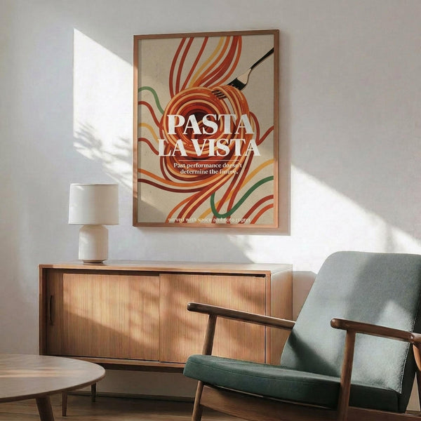 May include: Framed retro poster with colorful pasta noodles swirling around a fork on beige background, displaying "PASTA LA VISTA" text. Shown in modern living room with mid-century wooden sideboard, sage green armchair, white ceramic lamp, and natural sunlight casting shadows on white walls.