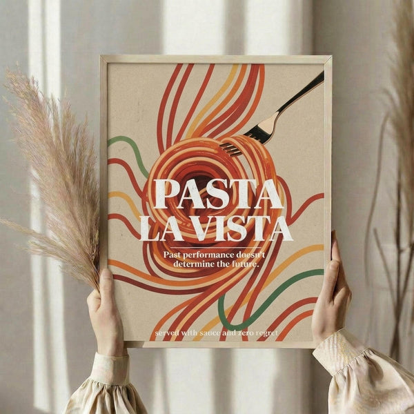 May include: Hands holding a framed retro-style poster featuring colorful swirling pasta noodles in orange, red, yellow and green strokes with "PASTA LA VISTA" text and "Past performance doesn't determine the future" subtitle. Light wood frame against neutral curtained background with dried wheat stems visible on left side.