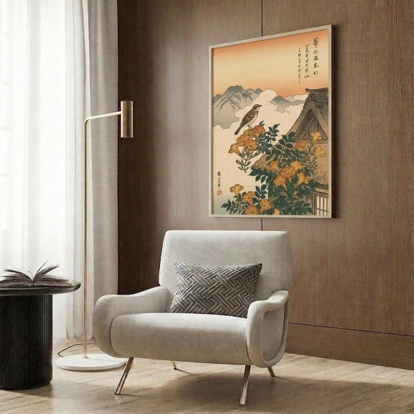 May include: Japanese woodblock print artwork featuring a bird perched on orange trumpet vine flowers with mountains in background, displayed in light wood frame on wood paneled wall above beige upholstered armchair with geometric pillow, beside brass floor lamp and dark side table with open book