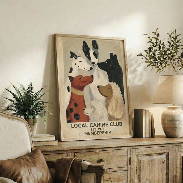 May include: Vintage-style poster featuring six illustrated dogs of different breeds and colors arranged in a group portrait, with text reading "Local Canine Club Est. 1976 Membership" at bottom. Framed artwork displayed on rustic wooden sideboard alongside potted plants, books, and ceramic vases in warm, neutral-toned living room setting.