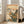 May include: Framed Japanese woodblock print featuring a small brown bird perched above orange trumpet vine flowers with green leaves, traditional thatched roof building, mountains and clouds in background with warm peachy sunset sky, displayed in light wooden frame leaning against white wall next to beige upholstered chair in bright modern living room with large windows.