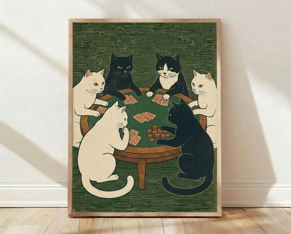 May include: Framed poster print in light wood frame showing six cats sitting around a green circular table playing cards. Art features vintage woodblock print style with cream and black cats holding playing cards, poker chips on table, against textured green background. Frame leans against white wall on light wooden floor with natural lighting casting soft shadows.