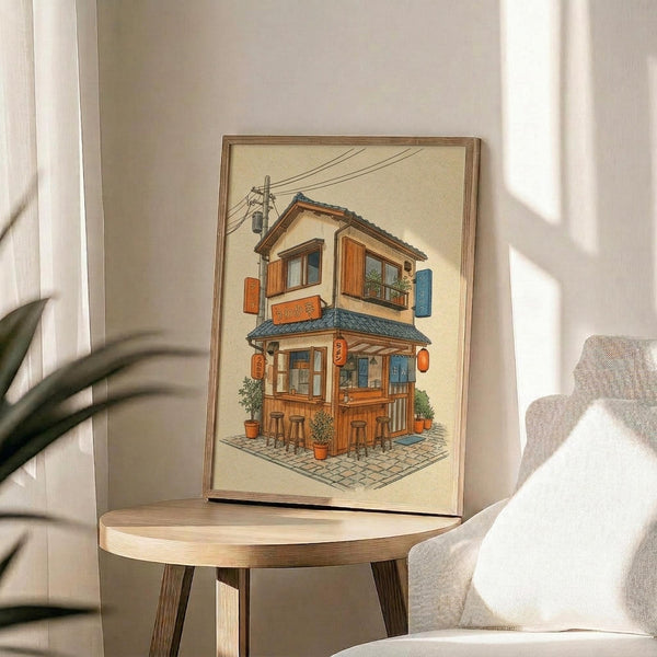 May include: Framed illustration of a two-story Japanese ramen shop with warm orange and blue wooden exterior, traditional tile roof, hanging lanterns, potted plants, and power lines above. Print displayed on round wooden side table next to beige upholstered chair with throw pillow in sunlit room with white walls and plant shadows.