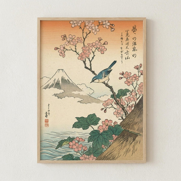 Framed Japanese woodblock print featuring a blue bird perched on cherry blossom branches with pink flowers and green leaves. Mount Fuji appears in the background with clouds, while water is visible in the foreground. The artwork has traditional Japanese calligraphy in the upper right corner and uses soft peachy-orange gradient colors in the sky. The print is displayed in a light wood frame against a white wall.
