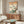 May include: Japanese woodblock print artwork hanging above wooden sideboard in modern living room. Print features Mount Fuji, pink cherry blossoms, blue bird, and Japanese text on cream background in thin frame. White curved chair and glass-top coffee table with walnut base visible. Warm natural lighting creates shadows on beige walls.