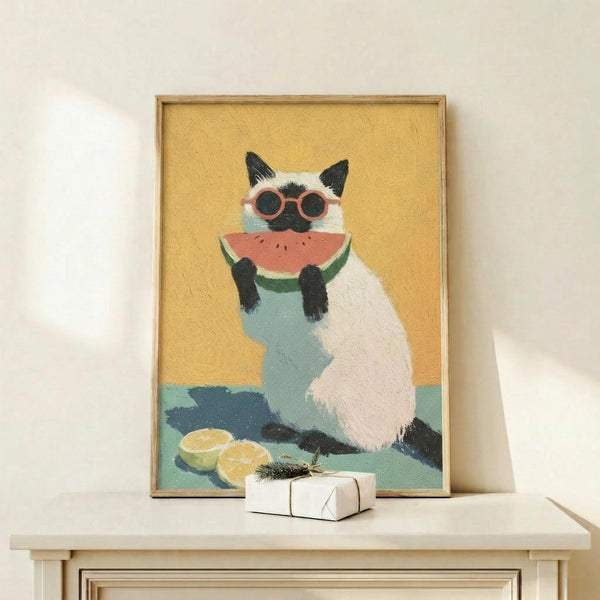 May include: Framed artwork showing a Siamese cat wearing pink sunglasses and light blue shirt, holding a watermelon slice. The cat has cream and dark brown coloring against a warm yellow background with teal accents. Orange slices sit at the bottom. The piece is displayed on a light wood surface next to a small white wrapped gift, leaning against a cream wall.