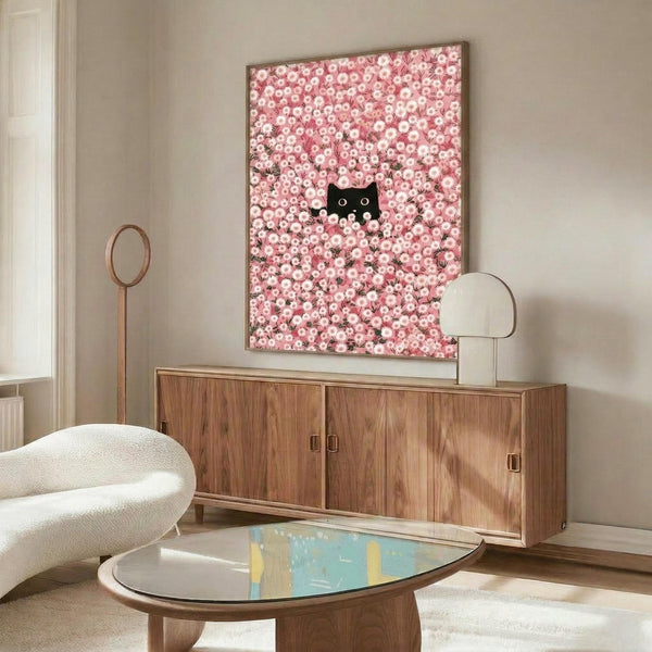 May include: Framed poster print featuring a black cat with white eyes peeking through dense pink and white daisy flowers, displayed above a mid-century modern wooden credenza in a minimalist living room with cream walls, white upholstered chair, and oval glass coffee table