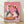May include: Framed poster print leaning against white wall on light wood floor. Artwork shows two white geese wearing sunglasses and colorful scarves at a dinner table with pizza and red wine glasses. Pink background with painterly brushstroke texture. Playing cards scattered on purple tablecloth. Whimsical anthropomorphic illustration in warm tones within natural wood frame.