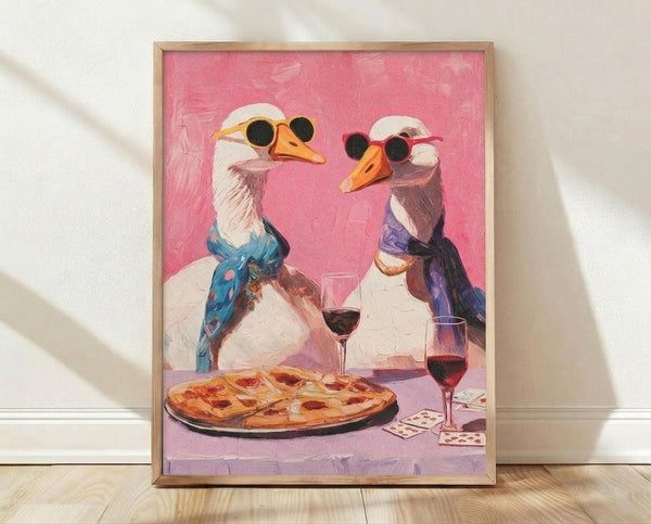 May include: Framed poster print leaning against white wall on light wood floor. Artwork shows two white geese wearing sunglasses and colorful scarves at a dinner table with pizza and red wine glasses. Pink background with painterly brushstroke texture. Playing cards scattered on purple tablecloth. Whimsical anthropomorphic illustration in warm tones within natural wood frame.