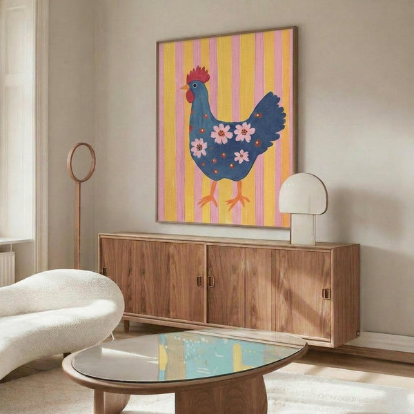 May include: Colorful folk art poster featuring a blue hen with red comb and pink flowers on its body, displayed against yellow and pink striped background. Shown framed on wall above walnut credenza in modern living room with white curved chair, glass coffee table, and table lamp.