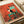 Vintage-style illustrated poster showing a black and white tuxedo cat sitting on a turquoise wooden chair against a vibrant coral red textured background. Several small dark birds perch on and around the chair. The artwork has a folk art aesthetic with warm, earthy tones and appears to be printed on canvas or textured paper, displayed in an open art book or portfolio.
