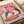 Two white geese wearing sunglasses sit at a dinner table sharing pizza and red wine against a pink background. The whimsical painting shows one goose in a blue scarf and the other in purple, with playing cards visible on the table. The artwork is displayed on white paper with a cream-colored ribbon beside it, photographed from above on a light wooden surface.