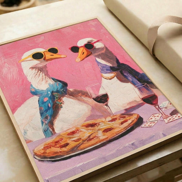 Two white geese wearing sunglasses sit at a dinner table sharing pizza and red wine against a pink background. The whimsical painting shows one goose in a blue scarf and the other in purple, with playing cards visible on the table. The artwork is displayed on white paper with a cream-colored ribbon beside it, photographed from above on a light wooden surface.