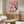 May include: Framed artwork showing two white geese wearing sunglasses and colorful scarves sitting at a table with pizza and wine glasses, displayed above a wooden credenza with brass handles. Modern living room setting features a white curved chair, oval glass coffee table, and neutral beige walls with natural lighting.