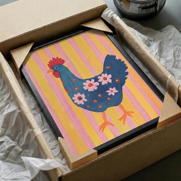 May include: Framed folk art print featuring a decorative blue hen with red comb and pink flowers on its body, set against yellow and pink vertical stripes. The black-framed artwork is being unpacked from a cardboard shipping box with protective tissue paper, surrounded by bubble wrap packaging materials on a neutral surface.