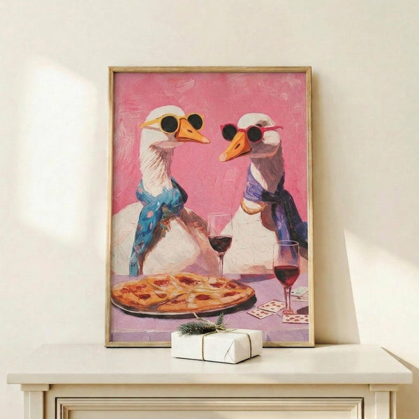 May include: Framed artwork showing two geese wearing Mickey Mouse ears sitting at a table with pizza and red wine glasses against a pink background. The painting has a whimsical, colorful style with the geese dressed in blue and purple clothing. The gold-framed print is displayed on a light wood shelf next to a small white wrapped gift with green twine, positioned against a cream colored wall.