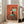 May include: Framed poster print leaning against white wall next to beige sofa in bright living room. Artwork shows black and white tuxedo cat sitting on turquoise wooden chair with three small dark birds perched on chair back and two birds on floor below. Background features warm orange-red textured wall. Print has light wood frame and textured canvas appearance.