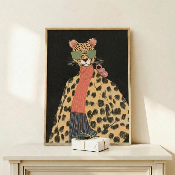 May include: Framed poster print featuring an anthropomorphic cheetah wearing green sunglasses, coral ribbed scarf, and leopard print coat against black background, displayed on light wood console table next to small white wrapped gift with evergreen sprig, against cream colored wall