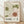 May include: Framed vintage-style botanical poster featuring two stylized flowers with dotted and striped petals in olive green and rust orange colors against cream background. Japanese and French text visible below artwork. Natural wood frame sits on light wooden floor against white textured wall with soft shadows.