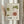 May include: Framed vintage-style Japanese exhibition poster featuring two large stylized flowers - one green daisy-like bloom and one coral-colored sunflower with detailed line work and dots. Japanese text and "JAPAN 1984" visible at bottom. Light wood frame displayed on neutral wall with dried pampas grass stems creating soft shadows in natural lighting.