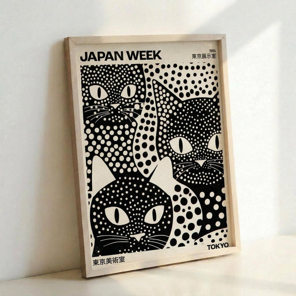 May include: Framed vintage poster with black and white polka-dotted cat faces in various sizes against cream background. Features Japanese text including "JAPAN WEEK," "1984," and "TOKYO." Light wood frame displayed leaning against white wall on white surface, showing artistic exhibition poster design with playful feline motifs created from dotted patterns.
