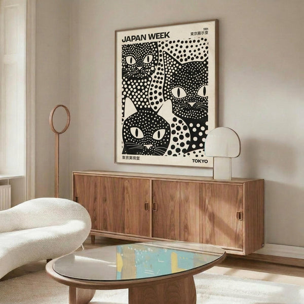 May include: Black and white polka dot cat poster in thin wooden frame hanging above walnut credenza in modern living room. Features three stylized cats with dotted patterns and whiskers against white background. Room has cream upholstered chair, brass floor lamp, oval glass coffee table, and white walls with natural lighting.