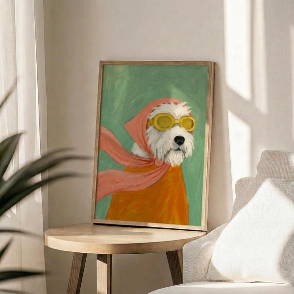 May include: Framed painting of a white fluffy dog wearing yellow goggles and a flowing pink scarf against a green background, displayed on a round wooden side table next to a beige upholstered chair with white pillow, near a plant and window with natural lighting in a modern living room setting.